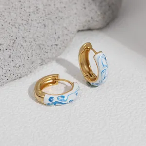 Macro view of gold hoop earrings with blue and white porcelain style enamel drip