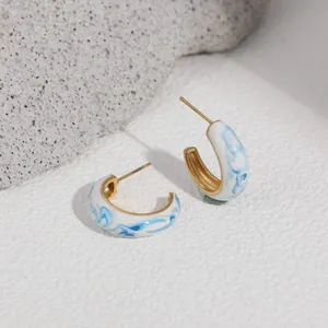 Close-up of blue and white enamel porcelain style hoop earrings with 18K gold plating