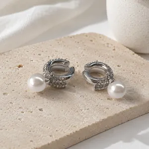 Vista detallada de ear cuffs plateados con pedrería y perlas blancas colgantes