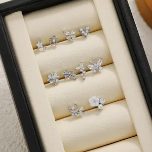 Close-up of zircon-inlaid silver ear studs with butterfly, star, and moon designs in box