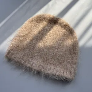 Close-up view of a fuzzy tan knitted beanie hat with soft natural window light shadows.