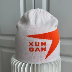 Primer plano de gorro de punto blanco con gráfico naranja y detalles de XUN GAN
