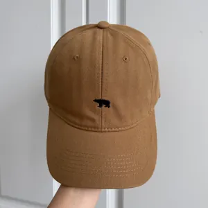 Détail d'une casquette de baseball marron avec une petite broderie d'ours noir devant