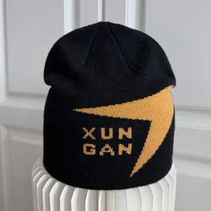 Detalle de gorro de punto negro con patrón de rayo amarillo y texto XUN GAN tejido