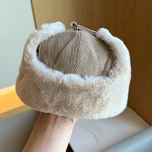 Close-up of a beige corduroy trapper hat with thick faux fur trim for winter warmth.