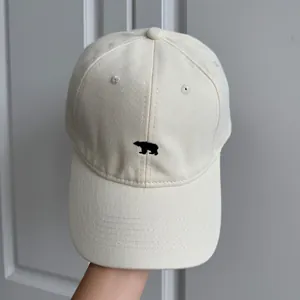 Gros plan d'une casquette de baseball crème minimaliste avec broderie d'ours noir