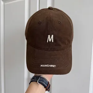 Detalle de gorra de béisbol marrón vintage con bordado de letra M blanca en la parte superior