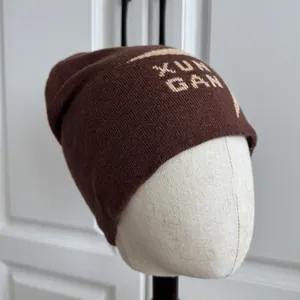 Primer plano de un gorro de punto marrón de invierno con el texto beige XUN GAN
