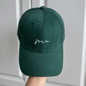 Gros plan d'une casquette de baseball vert foncé avec broderie cursive blanche 'me'