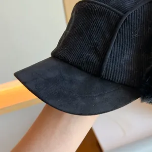 Close-up of black corduroy earflap hat showing brim and fabric texture.