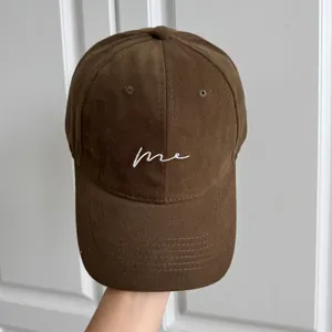 Gros plan d'une casquette de baseball marron avec broderie 'me' blanche style épuré.