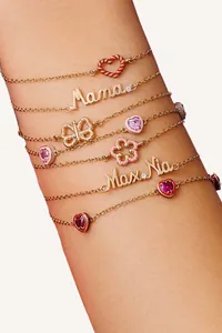 Close-up of stacked 18K gold plated stainless steel bracelets with heart and flower charms.