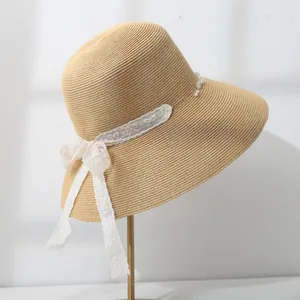 Detail of women's straw sun hat featuring elegant lace bow and delicate pearl accents