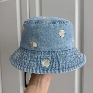 Detail view of light blue denim bucket hat featuring golden shell embroidery