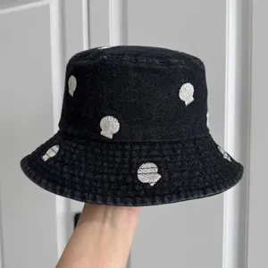 Detailed view of a black denim bucket hat featuring delicate white shell embroidery patterns