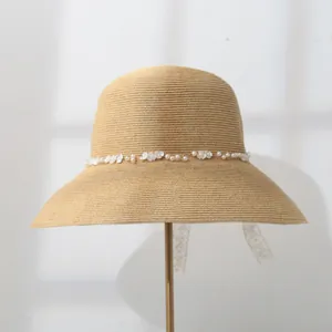 Detail view of a straw sun hat with wide brim and pearl shell flower embellishment.