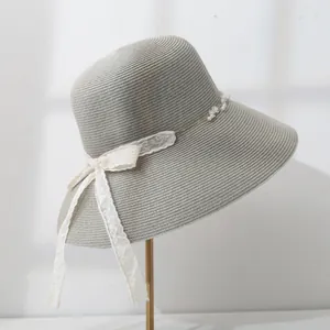 Detailed side view of a grey wide-brim straw sun hat with lace bow and pearl trim