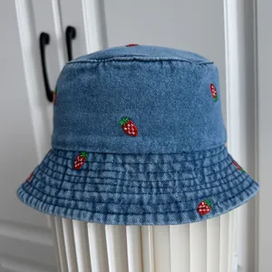 Detailed close-up of strawberry embroidery on a blue denim bucket hat for summer