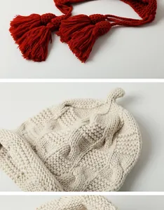 Detailansicht der handgestrickten Wintermütze mit roten Quasten und cremiger Wollstruktur