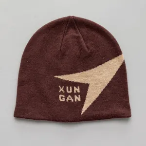 Primer plano de un gorro de punto marrón con logo XUN GAN y patrón geométrico