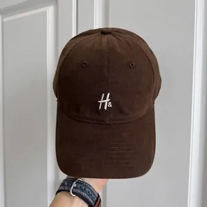 Primer plano de una gorra de béisbol retro marrón oscuro con bordado blanco de H y ampersand