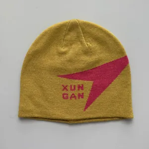 Vista detallada de gorro de punto mostaza con patrón geométrico rosa y logotipo