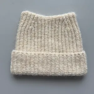 Close-up of beige knitted beanie with cute cat ear design and soft ribbed texture.