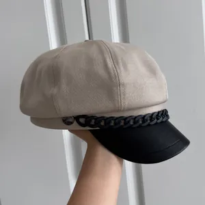 Detailansicht einer beige Schiebermütze mit schwarzer Krempe und Zierkette in der Hand