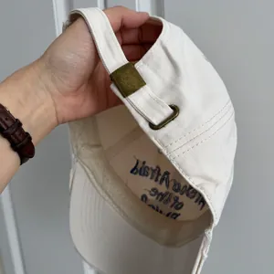 Détail de la boucle de réglage en métal sur une casquette de baseball écrue brodée.