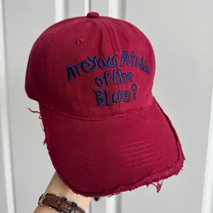 Détail d'une casquette de baseball bordeaux avec slogan brodé en bleu et bords usés
