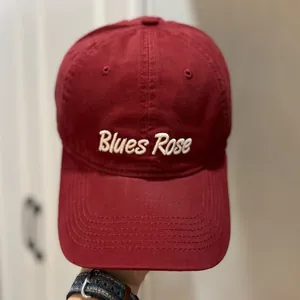 Gros plan d'une casquette de baseball bordeaux avec broderie blanche Blues Rose au front