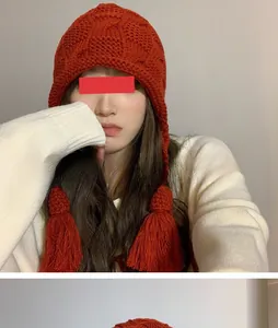 Detailaufnahme einer roten handgestrickten Wintermütze mit Ohrenklappen Quasten und Zopfmuster