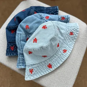 Detailed macro shot of three denim bucket hats featuring vibrant red lobster embroidery detail