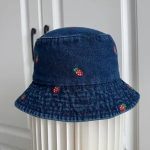 Detailed view of dark blue denim bucket hat with cute red strawberry embroidery