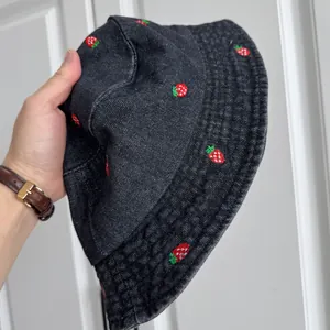 Detailed view of dark washed denim bucket hat with red strawberry embroidery patterns