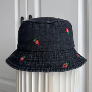 Detailed close-up view of a dark denim bucket hat featuring cute embroidered strawberry patterns.