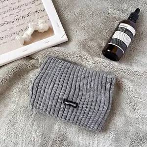 Dettaglio ravvicinato di fascia in maglia a coste grigia con patch SSHIEE su fondo soffice