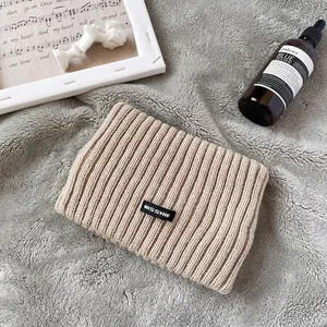 Dettaglio della fascia in maglia beige con patch MISSHIE su sfondo morbido e caldo