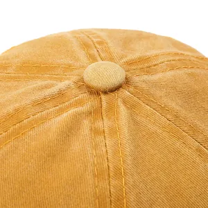 Close-up of the stitched crown and top button on a mustard yellow baseball cap.