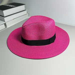 Close-up of fuchsia straw Panama hat with black ribbon band on minimalist background.
