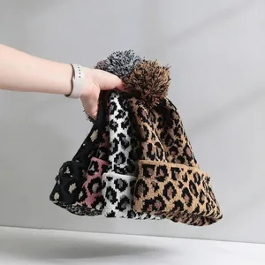 Detailed view of leopard print knit beanies with fuzzy pom-poms in four colors.