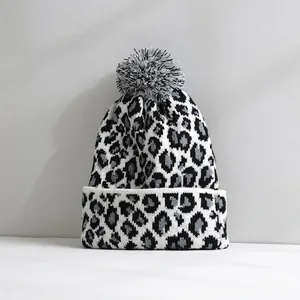 Detailed view of a leopard print knit beanie with a grey and white pompom on top.