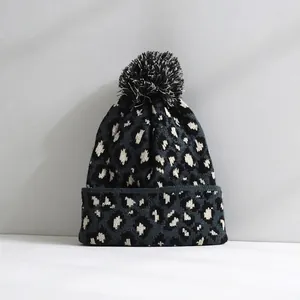 Front detailed view of a leopard print knitted beanie featuring a large soft pom-pom