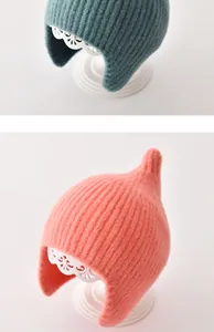 Detailweergave van gebreide babymutsen met oorkleppen in groenblauw en koraalroze.