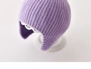 Gedetailleerd zicht van een paars gebreid babymutsje met oorflappen op een standaard.