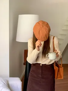 Berretto retrò in stile britannico arancio-marrone indossato in un ambiente accogliente.