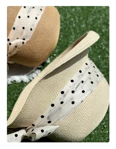 Dettaglio di un cappello di paglia intrecciato con nastro a pois e targhetta in metallo