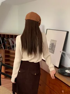 Vista posteriore di una donna con berretto vintage marrone in una stanza biblioteca accogliente