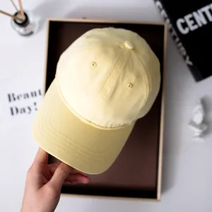 Draufsicht-Detail einer hellgelben einfarbigen Baumwoll-Basecap, präsentiert in einer Geschenkbox