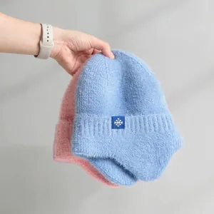 Close-up detail of soft fuzzy knit beanies with ear flaps and snowflake patch design